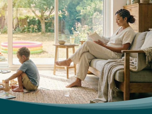 Living room with large windows facing the garden. Children play on a rug while a person reads on the sofa. Zehnder residential ventilation ensures air exchange.