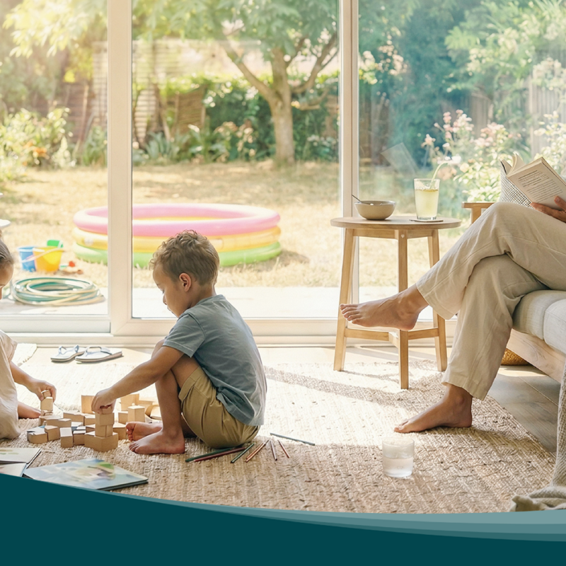 Living room with large windows facing the garden. Children play on a rug while a person reads on the sofa. Zehnder residential ventilation ensures air exchange.