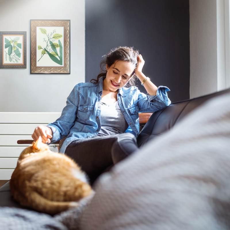 Beautiful young woman relaxing on sofa with her cat in living room.